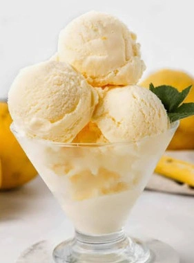 Une coupe en verre remplie de boules de glace au citron maison décorée de feuilles de menthe fraîches